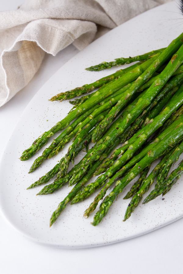 a serving platter with roasted asparagus on it, napkin on left.