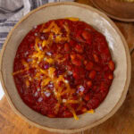 square crop looking down into a big bowl of chili topped with cheddar cheese and red onions.