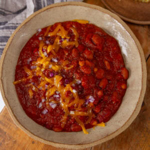 square crop looking down into a big bowl of chili topped with cheddar cheese and red onions.