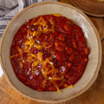 square crop looking down into a big bowl of chili topped with cheddar cheese and red onions.