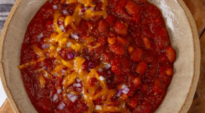 square crop looking down into a big bowl of chili topped with cheddar cheese and red onions.