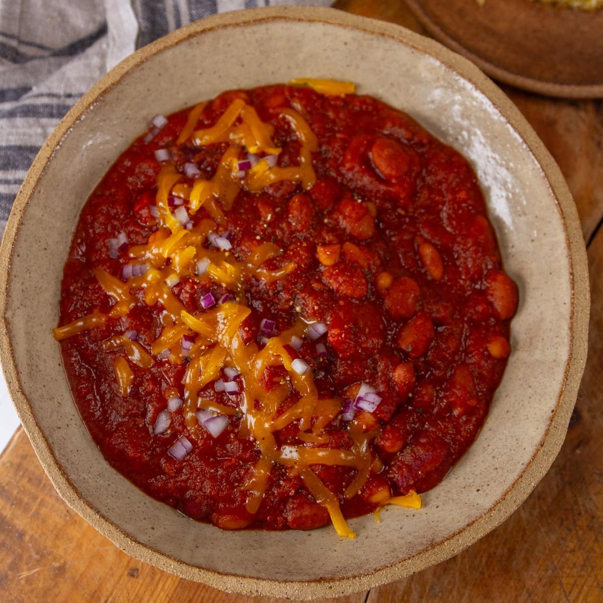 square crop looking down into a big bowl of chili topped with cheddar cheese and red onions.