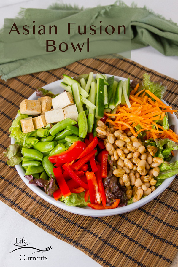 Asian Fusion Bowl Salad with lots of veggies, beans, tofu in a white bowl on a bamboo mat with a green napkin