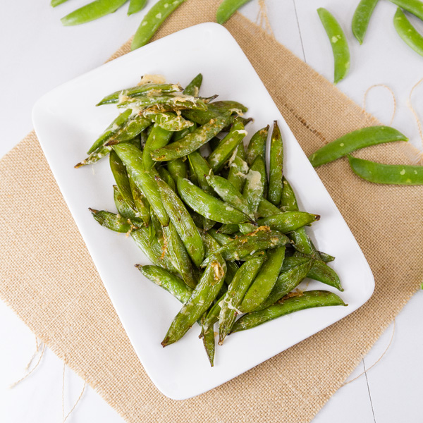square crop of Air Fryer Parmesan Sugar Snap Peas on a white plate with brown fabric in back