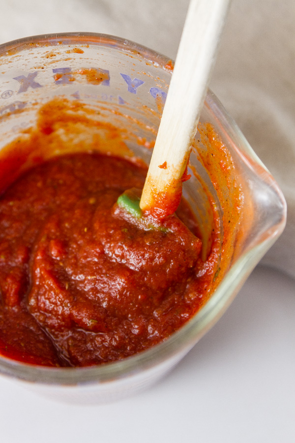 Pizza sauce in a glass pyrex measuring cup with a spoon 