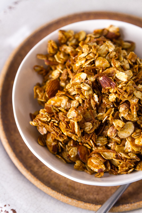 Homemade Granola Recipe served in a white bowl on a brown plate with a spoon on the right