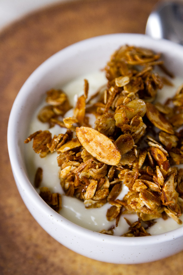 Homemade Granola Recipe served over yogurt in a white bowl on a brown plate 