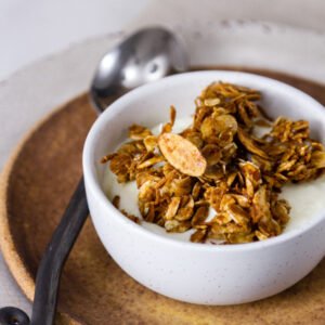 Homemade Granola Recipe in a white bowl served over yogurt, with a spoon on the left