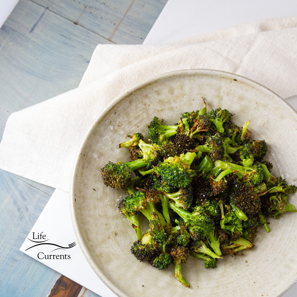 square crop top down of Air Fryer Roasted Broccoli in a white bowl on a white cloth with a blue counter top