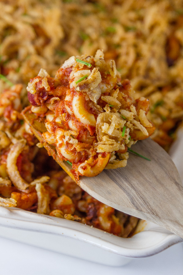 chili mac in the casserole dish being served with a wooden spoon