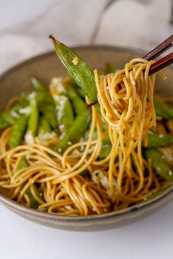 cooked snap peas served on Asian noodles picked up with chopsticks.