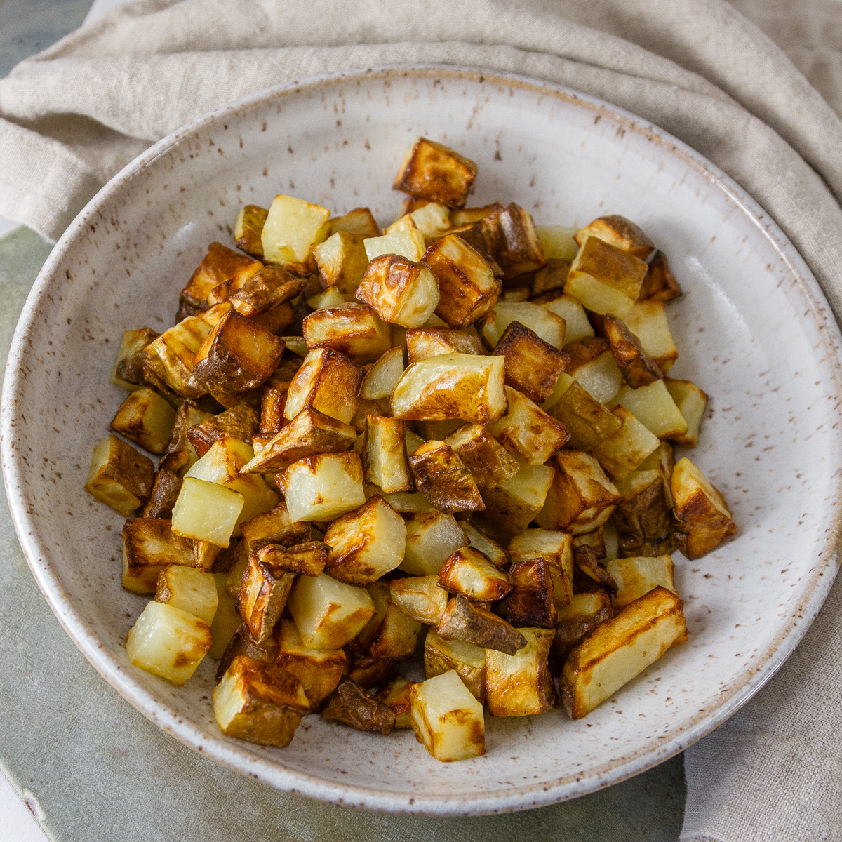 a white bowl filled with cubed cooked potatoes and a cloth napkin in the background.