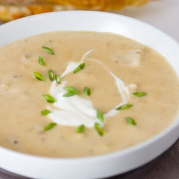 a bowl of Pepper Jack Potato Soup with a sour cream and chive garnish and bread slices in the background