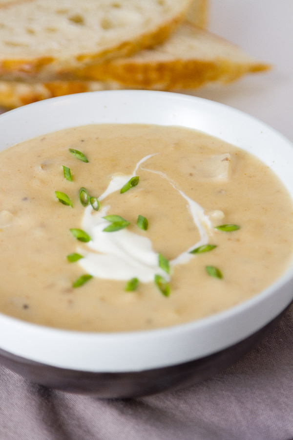 Rich and creamy, perfect comfort food. This Pepper Jack Potato Soup (or is it a chowder?) is so good and so easy to make. This is one your family will ask for again and again. a bowl of Pepper Jack Potato Soup with a sour cream and chive garnish and bread slices in the background