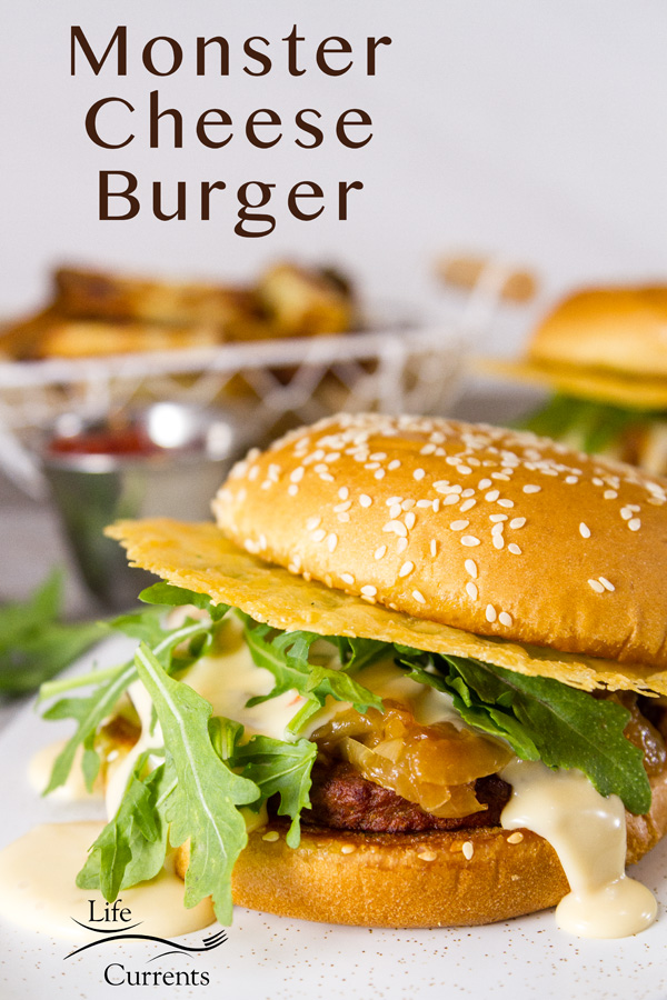 A close up of the Monster Cheese Burger with another burger and fries with ketchup in the background, title on the upper left 