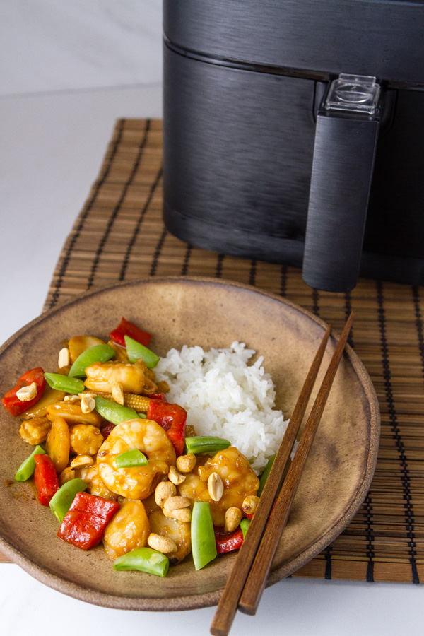 Kung Pao Shrimp in a bowl with rice in front of the air fryer on an Asian mat