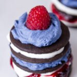 Patriotic Icebox Cakes on a white plate - cookies, whipped cream, jam, and a rasberry all stacked up