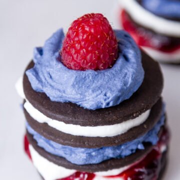 Patriotic Icebox Cakes on a white plate - cookies, whipped cream, jam, and a rasberry all stacked up
