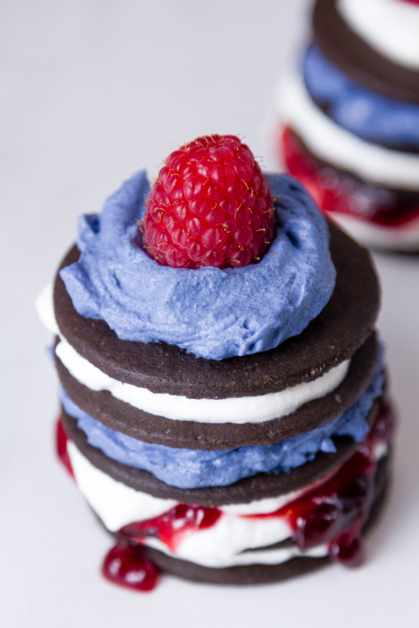 Patriotic Icebox Cakes on a white plate - cookies, whipped cream, jam, and a rasberry all stacked up 