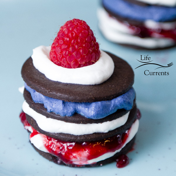 two Patriotic Icebox Cakes - one if the front and one in the back on a blue plate. cookies stacked with whipped cream, jam, and berries 