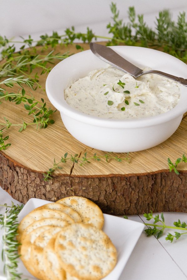 Garlic and Herb Cheese Spread in a white bowl with a knife and some crackers in the lower left