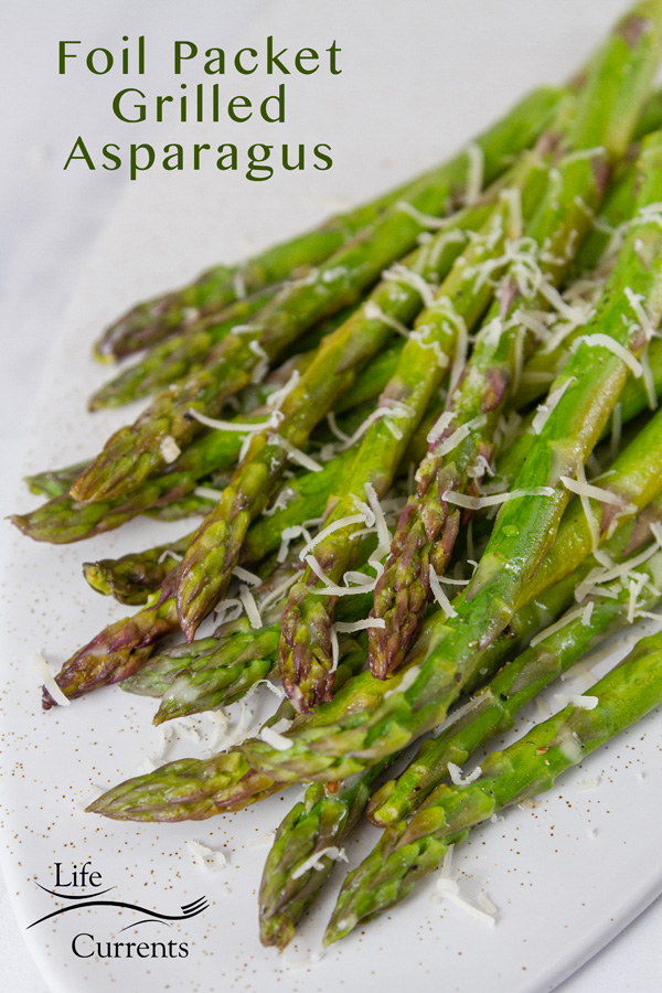 grilled asparagus on a white plate sprinkled with grated Parmesan cheese. Title in the top left: Foil Packet Grilled Asparagus