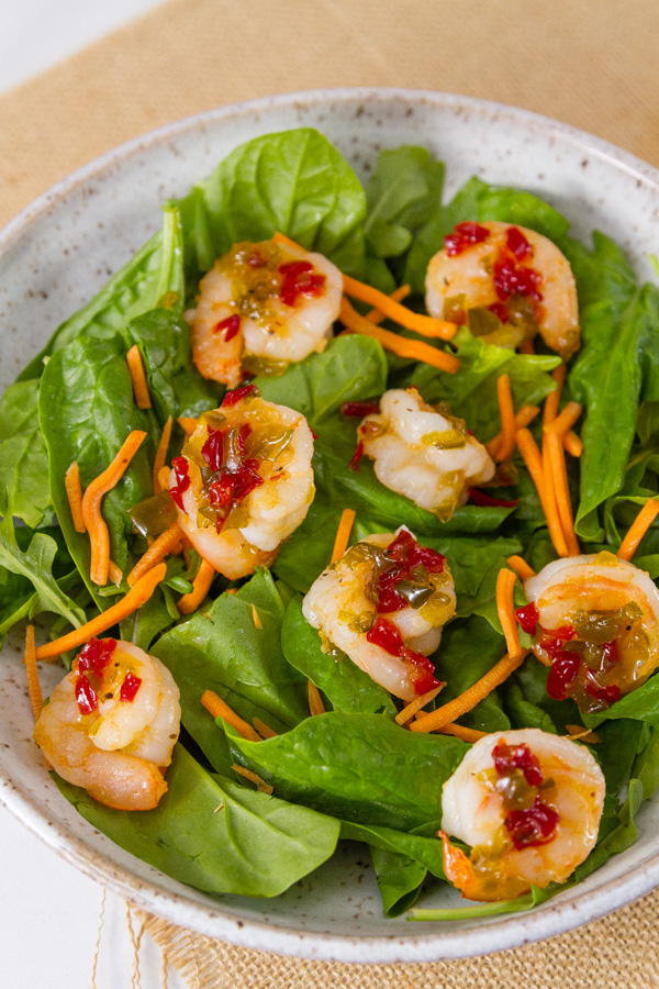 Pepper Jelly Shrimp on a bed of fresh spinach with shredded carrots in a white bowl 