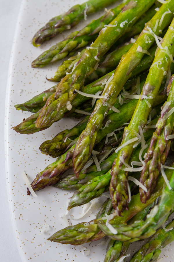 grilled asparagus arranged on a white platter topped with Parmesan