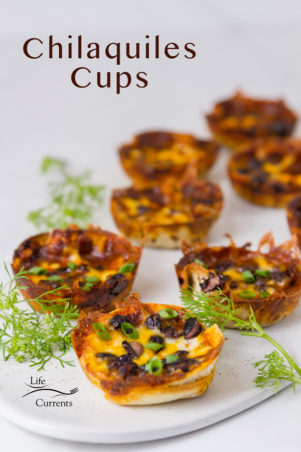 little individual cups made from tortillas and filled with sauce, black beans and cheese. Topped with green onions, and garnished with cilantro on a white platter with the title on the upper left: Chilaquiles Cups