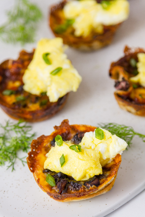 Chilaquiles Cups: filled with enchilada sauce, cheese, and black beans topped with scrambled eggs, green onions served with cilantro garnish