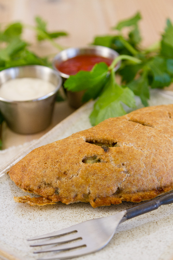a turnover on a dark plate served with dipping sauces with parsley in the background