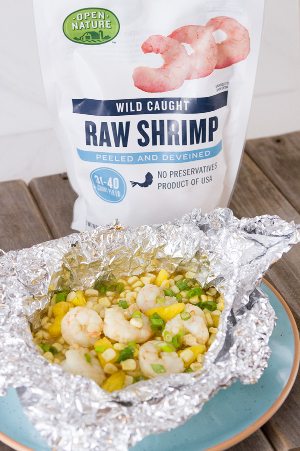 Foil Packet Caribbean Shrimp still in the foil on a blue plate with a bag of Open Nature Raw Shrimp in the background