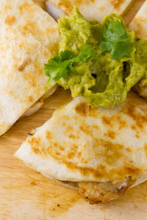close up on a shrimp quesadilla wedge served with guacamole and garnished with cilantro