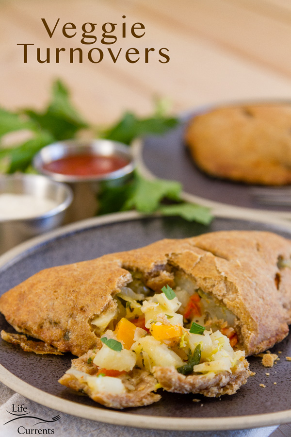 a savory vegetable turnover that's been cut open so you can see the filling on a dark plate with marinara and Alfredo dipping sauces in the background. Title on image: Veggie Turnovers