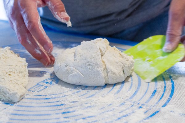 shaping bread dough using a pastry scraper and a measuring mat
