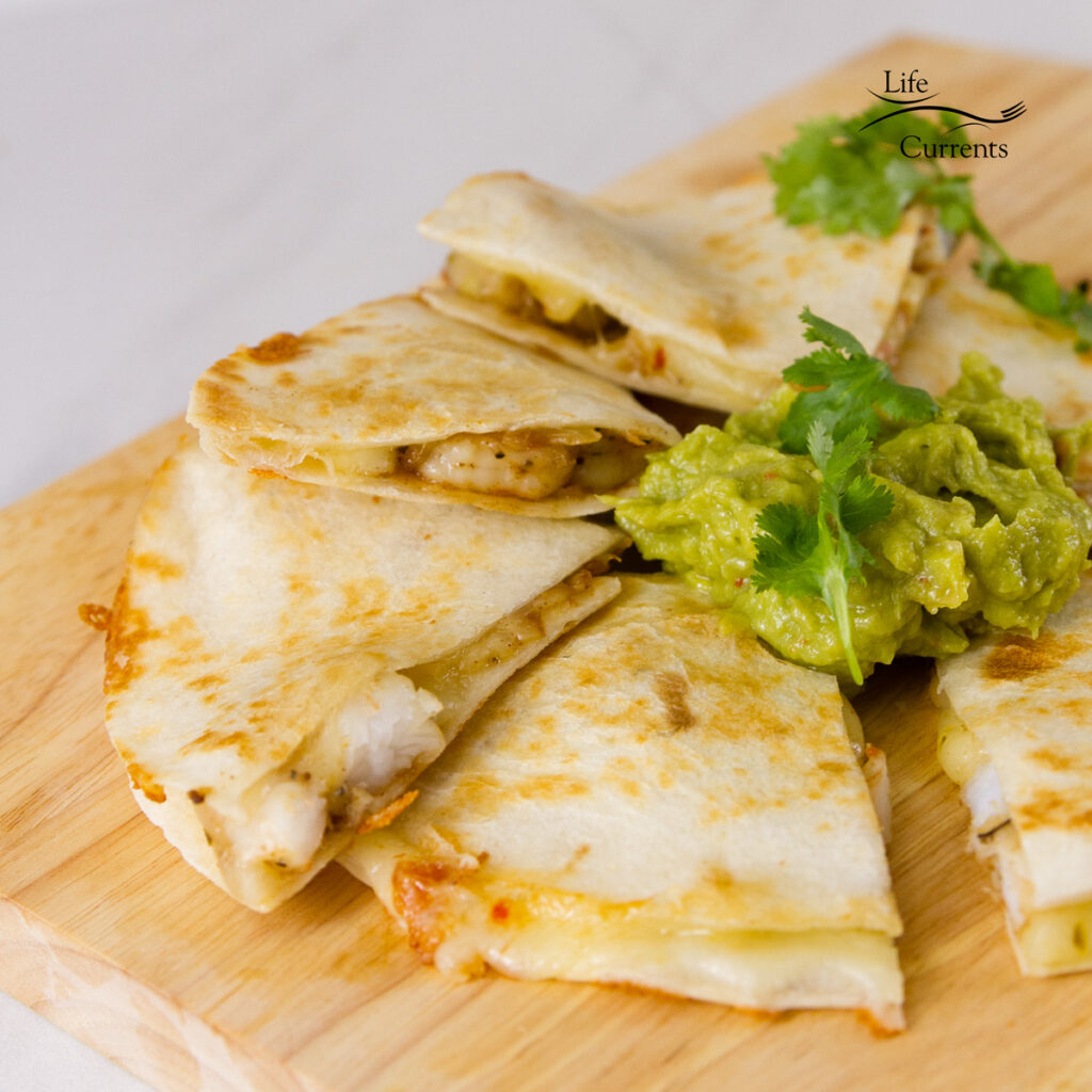 square crop of quesadillas on a wooden cutting board served with guacamole and cilantro 