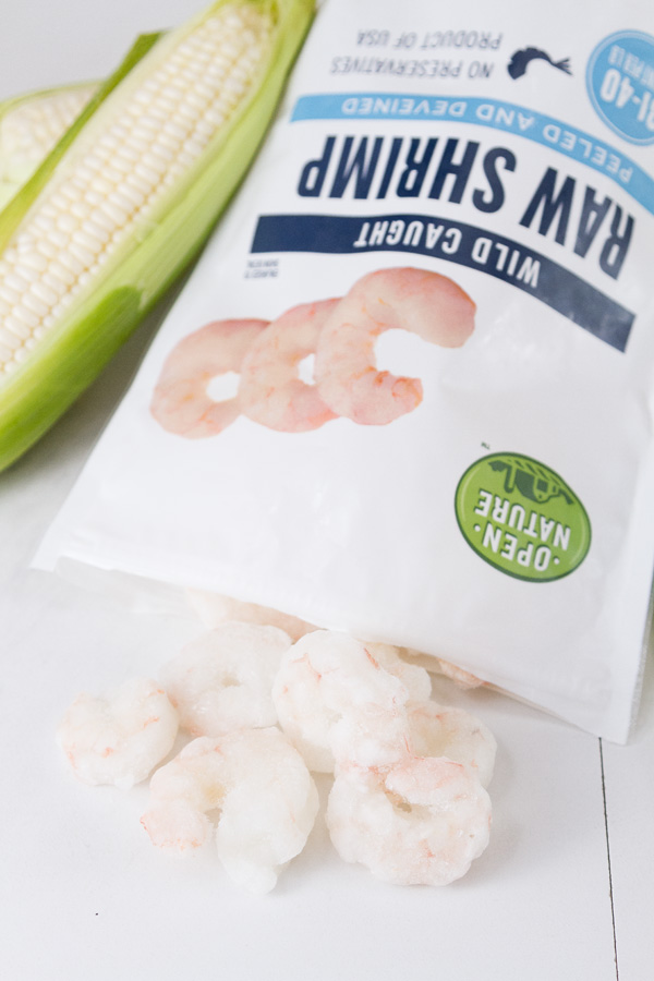 A bag of Open Nature Raw Shrimp open and the shrimp coming out of it with an ear of corn in the background