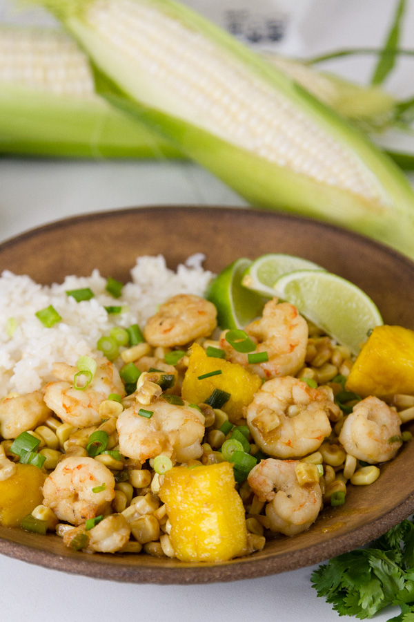 Foil Packet Caribbean Shrimp  served with coconut rice on a brown bowl with aears of corn in the background