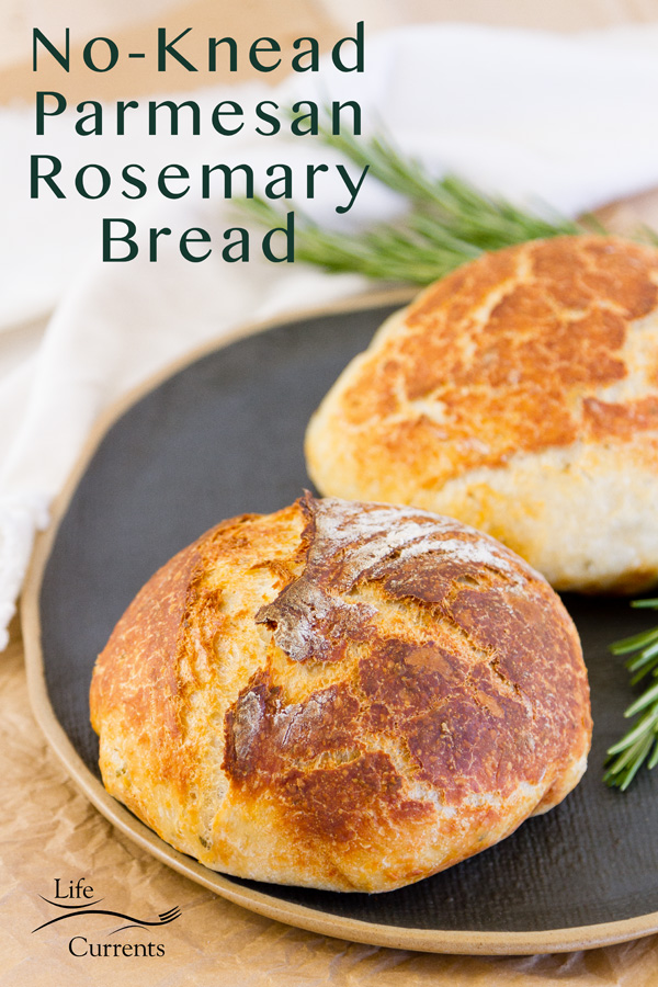 two loaves of No-Knead Parmesan Rosemary Bread on a drk platter with a white cloth and fresh roasmary around