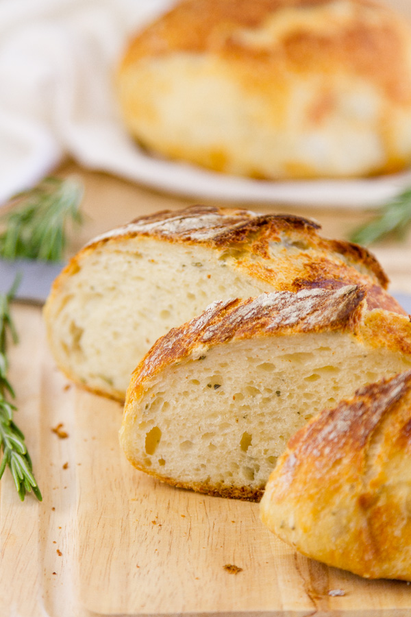 sliced rosemary Parmesan bread on a cutting borad with a second loaf in the background