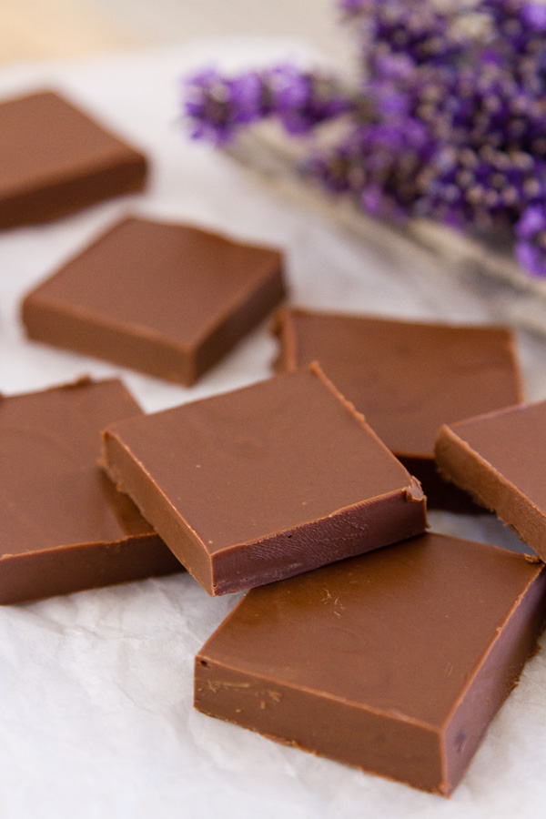 pieces of Two Ingredient Peanut Butter Chocolate Fudge on parchment paper with lavender in the back
