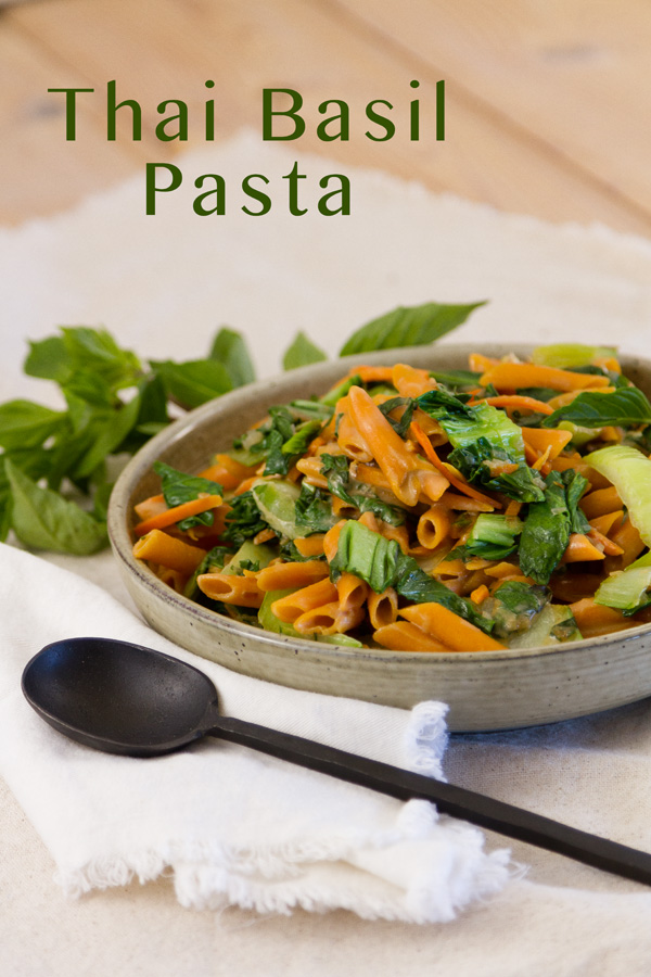 A bowl of Thai Basil Pasta with the title and a black serving spoon on a napkin