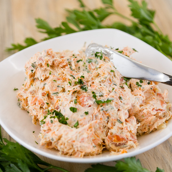 a white bowl with salmon pate, a knife, and fresh parsley 