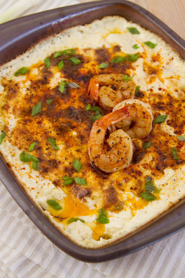 Shrimp and cheese dip in a square clay baking dish with shrimp on top garnished with green onions