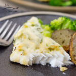 Parmesan halibut on a plate next to roasted potatoes and broccoli and a fork.