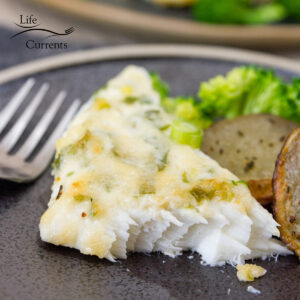 Parmesan halibut on a plate next to roasted potatoes and broccoli and a fork.