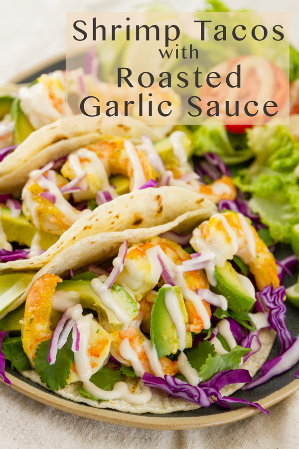 Title on image: Shrimp Tacos with Roasted Garlic Sauce. Shrimp tacos on a plate with a side salad