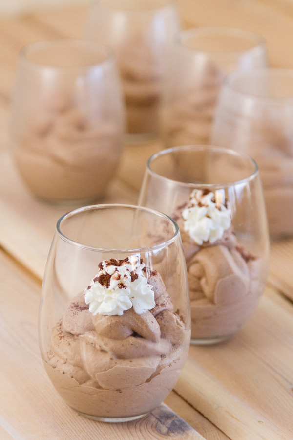 several glasses filled with mousse, two are toped with whipped cream and cocoa