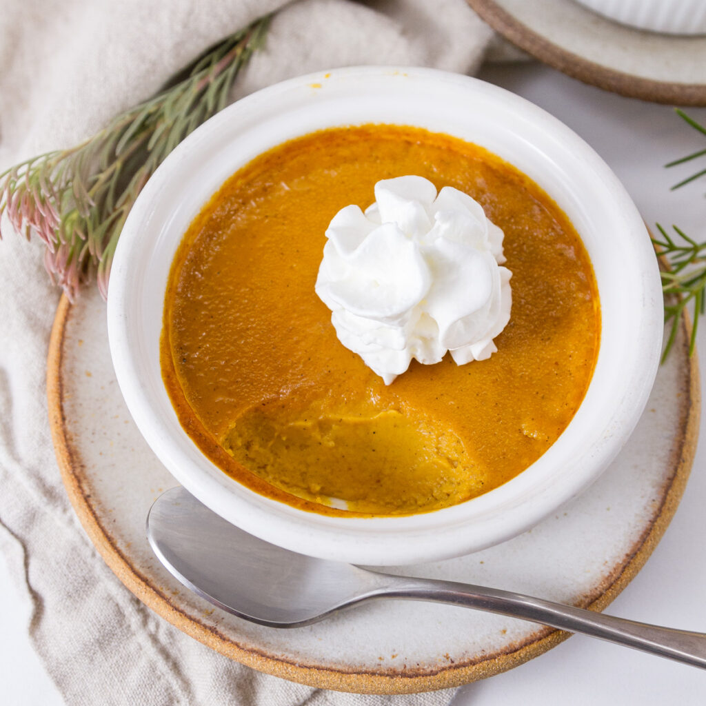 square crop of pumpkin pie in custard cup on a plate with a spoon