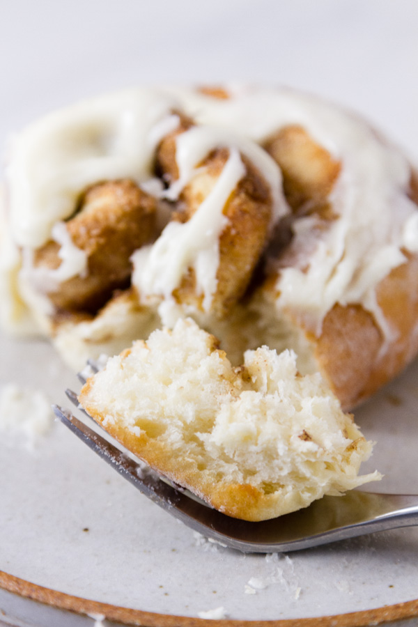 a fork full of a cinnamon roll on a plate